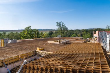 Yeşil yaz manzarasında, mavi gökyüzü arka planında inşaat alanındaki çelik ağı güçlendirmek. İnşaat halindeki evin betonunu güçlendirmek için paslı kahverengi demir ızgara. Ferrobeton demiri.