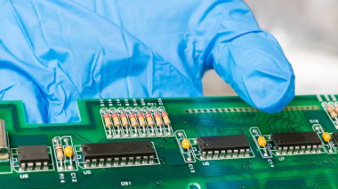 Yeşil baskılı devre kartındaki elektronik bileşenler insan elinin mavi eldiveni. Bilgisayar klavyesinin PCB detayında standart renk kodlu siyah IC çipleri, kapasitörler veya dirençlerin kapatılması.