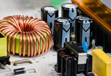 Toroidal çekirdek indüktörü, trafo ya da elektrolitik kondansatörler. Bakır telle sarılmış bobin yakın plan. Elektrik bileşenleri beyaz baskılı devre kartı üzerinde geçiş modu güç arzı.