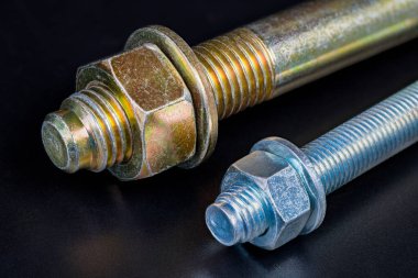 Galvanize cıvatalar üzerindeki metal fındıklar ve yıkayıcılar siyah arka planda yansıtılıyor. Betona dönüşecek iki kama genişletme çapasının sonları. Paslanmayı önlemek için koruyucu çinko veya krom kaplama.