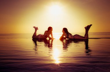 İki güzel kız gün batımında sonsuz havuzda eğleniyor. Maldivler.