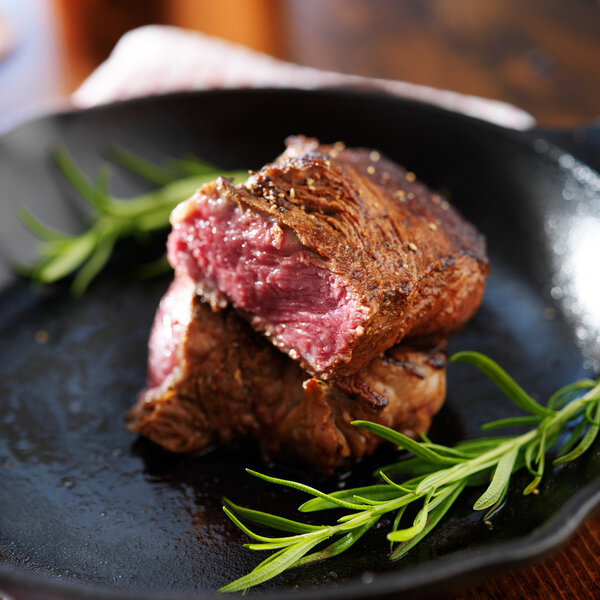 Rare steak cut in half on iron skillet with rosemary
