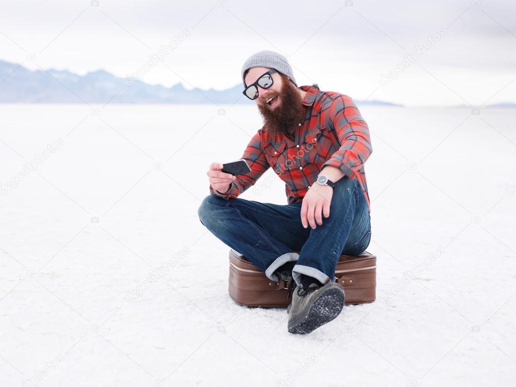 beard hipster with smart phone and suit case in the salt flats looking for directions