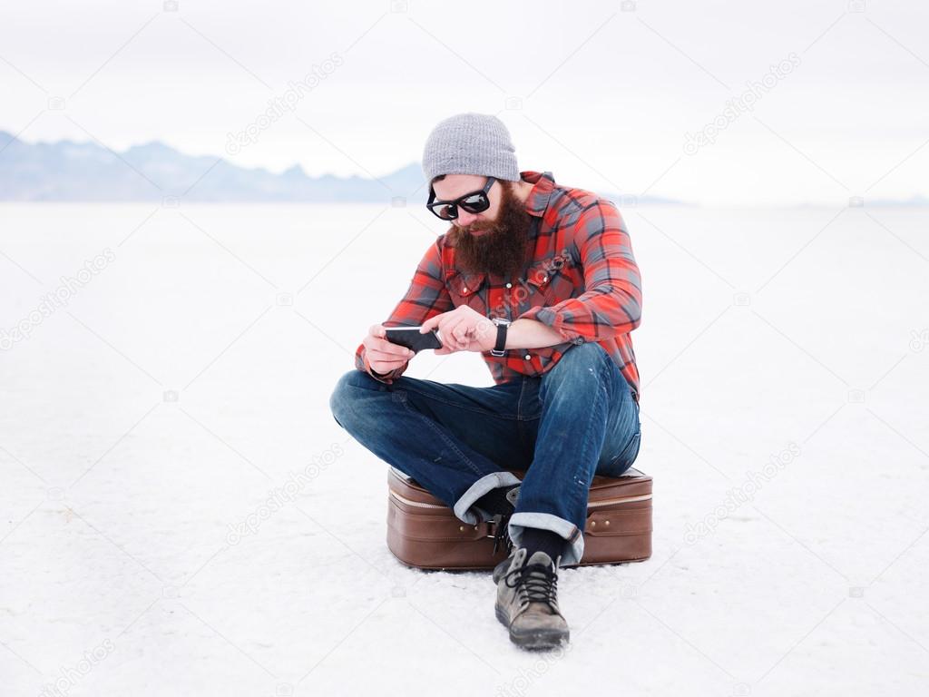 bearded hipster with smart phone and suit case in the salt flats