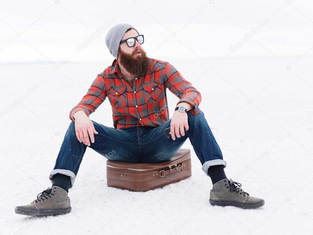 bearded hipster sitting on suitcase in salt flats waiting