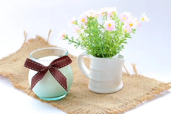 Glass of milk with ribbon on sack over white. — Stock Photo, Image