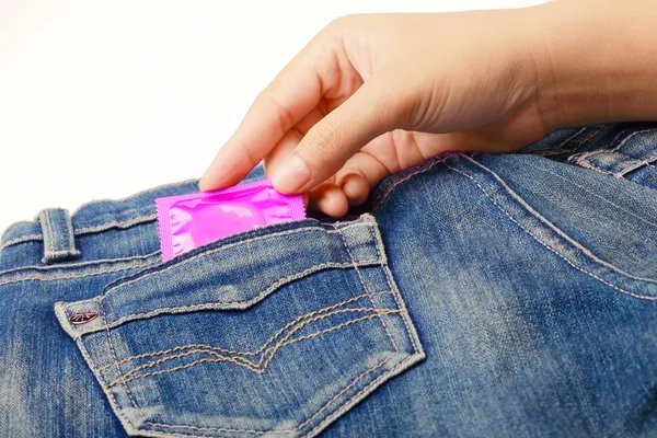 Ženská ruka s růžovým kondom v džínách kapsy na bílém — Stock fotografie