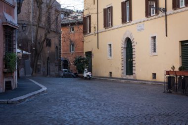 Görüntüde çeşitli sarı, pas ve gri tonlarında yıpranmış cepheli eski binalar yer alıyor. Roma