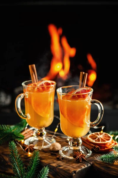 Mulled cider glasses on the background of fireplace fire. Hot mulled spiced apple cider cocktail for winter or autumn time.