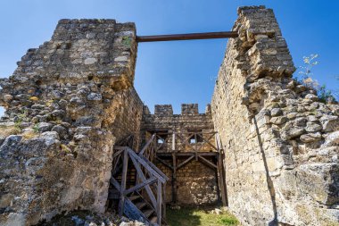 Bulgaristan 'ın Cherven Kalesi' ndeki ortaçağ savunma kulesinin yakın plan görüntüsü, yıpranmış taş duvarlar, kısmi siperler ve berrak mavi gökyüzünün altındaki ahşap merdiven yapılarını gösteriyor..