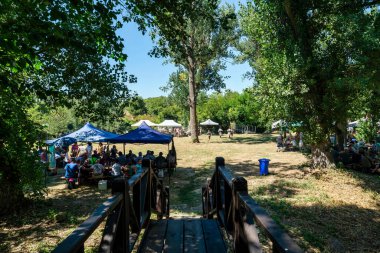 İvanovo, Bulgaristan - 9 Ağustos 2025: Kamu etkinliği, Rusenski Lom Doğa Parkı 'ndaki Ivanovo Rock-Hewn Kiliseleri yakınlarındaki gölgeli bir ormanda renkli çadırlarla, masalarda oturan insanlar ve parlak bir yaz atmosferinde gerçekleşti.