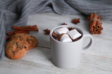 Bir fincan çikolatalı, baharatlı, kurabiyeli, beyaz ahşap arka planda gri örülü eşarp. Kış içkisi konsepti. Baharatlı kakao, menü, yakın plan, boşluğu kopyala