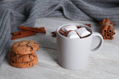 Soluk bir fincan çikolatalı marşmelov, baharatlar, kurabiyeler, beyaz ahşap arka planda gri örülü eşarp. Kış içkisi konsepti. Baharatlı kakao, menü, yakın plan, boşluğu kopyala