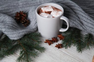 Marşmelovlu sıcak çikolata, baharatlar, gri örgü ekose, köknar ağacı dalları, beyaz ahşap masadaki koniler. Kış ve Noel konsepti. Baharatlı kakao, yeni yıl, yakın çekim, kopyalama alanı