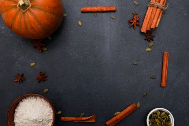 Tarçın baharatları, portakallı taze balkabağı, tohumlar, fırın için un siyah masada. Sonbahar menüsü ya da sonbahar ev yapımı yemek konsepti. Ev mutfağı, Şükran Günü, üst manzara.