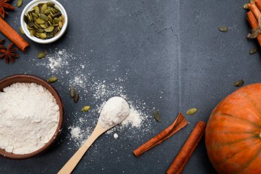 Tarçın baharatları, portakallı taze balkabağı, tohumlar, fırın için saçılmış un siyah masaya saçılmış vaziyette. Sonbahar menüsü ya da sonbahar ev yapımı yemek konsepti. Ev mutfağı, Şükran Günü, üst manzara.