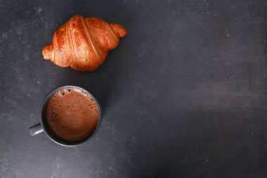 Taze pişmiş kruvasan, koyu beton masada bir kupa ekspresso. Bir fincan sıcak kahve, çörekler, yakın çekim. Yemek, Fransız kahvaltısı, sabah menüsü, kafe konsepti. Üst görünüm, alanı kopyala