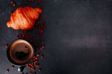 Taze kruvasan, koyu beton masada bir fincan koyu kahve. Bir fincan sert Americano, Espresso, fasulye, Fransız dürümü, yakın çekim. Yemek, kahvaltı, fırın, günaydın konsepti. Üst görünüm