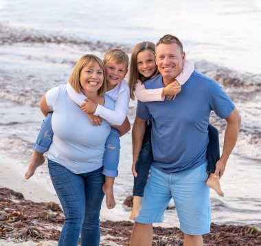 Dört kişilik mutlu bir ailenin açık hava portresi, anne, baba ve çocuklar, plajda kucaklaşıp birlikte eğleniyorlar. Mutlu anlar, tatiller ve tatil portresi konsepti.