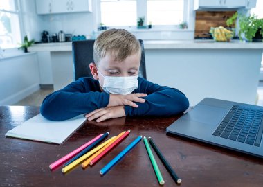 Yüz maskesi takmış okul çocuğu online eğitim hakkında sanal ders izliyor. Evde kendini soyutlanmış ve sıkılmış hissediyor. COVID-19 salgını nedeniyle uzak öğrenim ve kapalı okullar ikinci dalga.