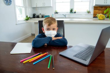 Yüz maskesi takmış okul çocuğu online eğitim hakkında sanal ders izliyor. Evde kendini soyutlanmış ve sıkılmış hissediyor. COVID-19 salgını nedeniyle uzak öğrenim ve kapalı okullar ikinci dalga.