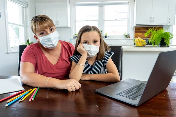 Stressed Mother helping bored daughter studying online lesson at home. Parent and child with face mask homeschooling during second lockdown, self isolation or School closures due to COVID-19 Outbreak.