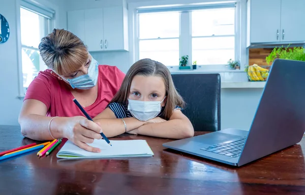 Stressed Mother helping bored daughter studying online lesson at home. Parent and child with face mask homeschooling during second lockdown, self isolation or School closures due to COVID-19 Outbreak.