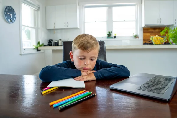 Sad school boy watching virtual lesson in online education classes feeling bored and depressed at home in self-isolation. COVID-19 second wave, quarantine, school closures and remote learning concept.