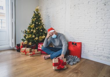 Maskeli üzgün bir adam Noel 'de yalnız başına evde yalnız başına yas tutuyor ve ailesini ve arkadaşlarını özlüyor. COVID-19 Kış tatili ve akıl sağlığı süresince karantina ve tecrit.