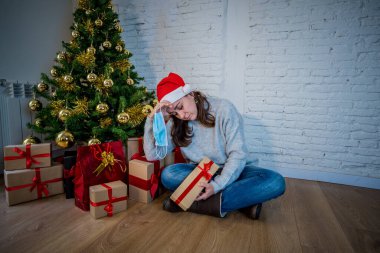 Maskeli üzgün kadın Noel 'de yalnız başına evde yalnız başına yas tutuyor ve ailesini ve arkadaşlarını özlüyor. COVID-19 Kış tatili ve akıl sağlığı süresince karantina ve tecrit.