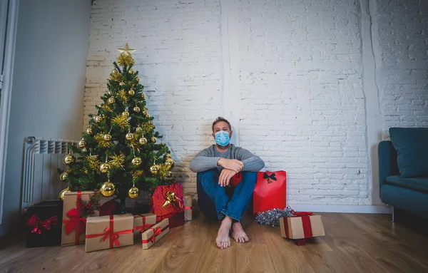 Sad man with mask home alone in self isolation at christmas feeling depressed mourning and missing family and friends. COVID-19 Lockdown and quarantine during winter holidays and mental health.