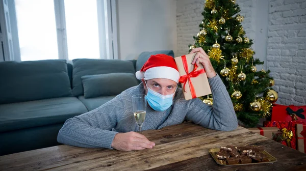 Sad man with mask home alone in self isolation at christmas feeling depressed mourning and missing family and friends. COVID-19 Lockdown and quarantine during winter holidays and mental health.