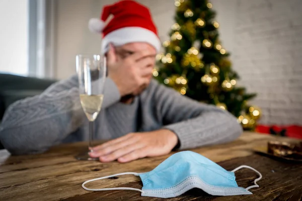 Conceptual image of hand sanitizer, champagne glass and out of Focus background of depressed man alone in self isolation at christmas. COVID-19 Lockdown and quarantine on holidays and mental health.