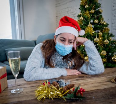 Maskeli üzgün kadın Noel 'de yalnız başına evde yalnız başına yas tutuyor ve ailesini ve arkadaşlarını özlüyor. COVID-19 Kış tatili ve akıl sağlığı süresince karantina ve tecrit.
