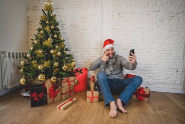 Mutlu adam evde yalnız başına telefon kullanarak sanal Noel videolarını kutluyor. Ailesini ve arkadaşını arıyor. Coronavirüs nedeniyle sanal tatil çevrimiçi Yeni normal ve sosyal mesafeler.