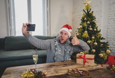 Mutlu adam evde yalnız başına telefon kullanarak sanal Noel videolarını kutluyor. Ailesini ve arkadaşını arıyor. Coronavirüs nedeniyle sanal tatil çevrimiçi Yeni normal ve sosyal mesafeler.