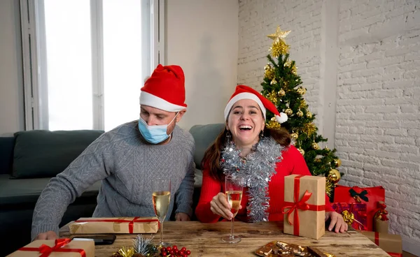 Webcam view of happy couple with face mask on video call celebrating virtual christmas and new year party at home in lockdown. COVID-19 social distancing, self isolation and online celebrations.