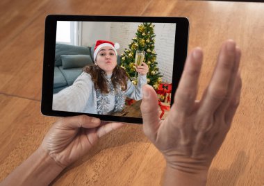 COVID-19 Sanal Noel Kutlaması. İnternetteki sanal noeli kutlayan videodaki kadınla ekran tableti resmi. Sosyal uzaklık, koronavirüs karantinası bayram kutlamaları.