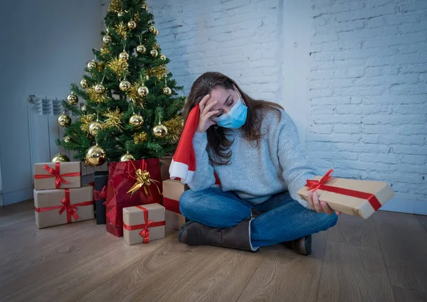 Sad woman with mask home alone in self isolation at christmas feeling depressed mourning and missing family and friends. COVID-19 Lockdown and quarantine during winter holidays and mental health.