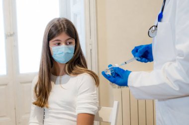 Doktor kliniğinde yüz maskesi takan genç bir kız hastaya koronavirüs aşısı yapan hemşire. İnsanlarda yapılan klinik deneylerden sonra bağışıklık, tıbbi tedavi ve Covid-19 aşı programı.