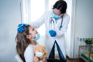 Hemşire Coronavirus enfeksiyonu için genç kızı test ediyor. Hızlı COVID-19 testi yapıyor. Doktor, enfeksiyon kapıp kapmadığını anlamak için çocuğa genizden örnek alıyor..
