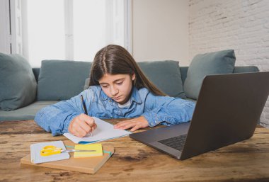 Bilgisayardaki mutlu genç kız evde internetteki sanal uzak sınıflarda ders çalışıyor çünkü lise son koronavirüs kilitlenmesi nedeniyle kapalı kalıyor. COVID-19, eğitim, çocuklar, E-öğrenme.