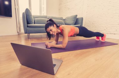 Evde çalışan genç, güzel Latin bir kadın bilgisayardaki beden eğitimi dersine bağlanmış. Kadın kişisel antrenör hocası zoom öğretim egzersizleri canlı yayın egzersiz sınıfında.