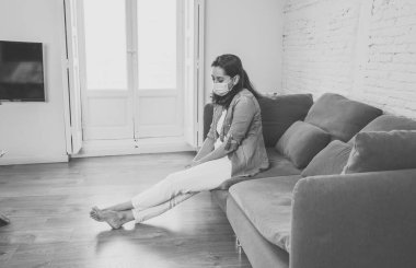 Oturma odasındaki kanepede koruyucu maskeli üzgün Latin kadın. Koronavirüs hapsi ve sosyal mesafeler yüzünden bunalımda ve yorgun hissediyor. Ruh sağlığı ve tecrit kavramı.