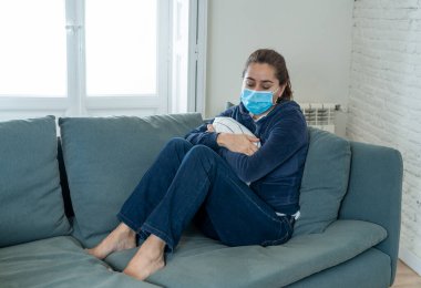 Oturma odasındaki kanepede koruyucu maskeli üzgün Latin kadın. Koronavirüs hapsi ve sosyal mesafeler yüzünden bunalımda ve yorgun hissediyor. Ruh sağlığı ve tecrit kavramı.