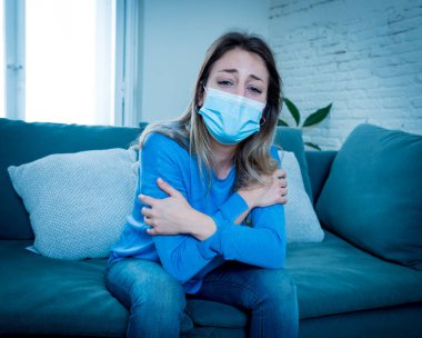 Oturma odasındaki kanepede koruyucu maskeli üzgün, yorgun ve endişeli bir kadın depresyon geçiriyor. Koronavirüs salgınından ve izolasyon konseptinden etkilenen akıl sağlığı.