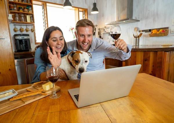 COVID-19 Stay safe Stay connected over winter holidays. Couple with dog pet in online video call cheering and celebrating christmas virtually with family during coronavirus second wave.