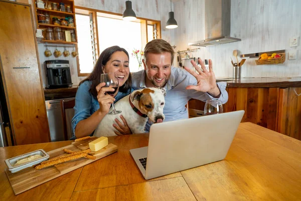 COVID-19 Stay safe Stay connected over winter holidays. Couple with dog pet in online video call cheering and celebrating christmas virtually with family during coronavirus second wave.