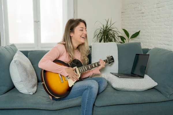 在网上音乐课上 女人用笔记本电脑弹电吉他 在学习摇滚音乐方面 女人们在观看视频教学时很开心 业余爱好和闲暇 社交活动中的虚拟活动 — 图库照片