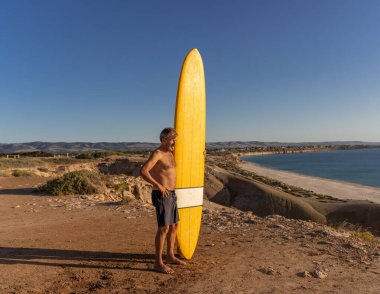 Çekici Avustralyalı olgun sörfçü gün batımında plajda kaliteli sörf tahtasıyla. Son sınıf öğrencisi sörf yapmaya döndüğü için mutlu. Açık hava sporları, aktif yaşlılar ve emeklilik hayatı..